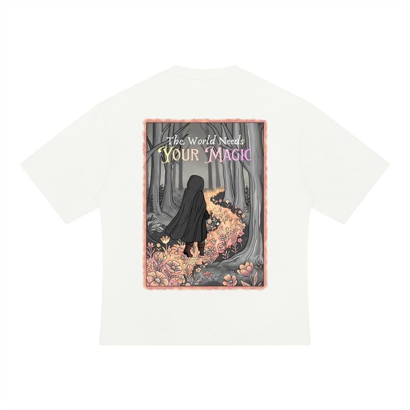 An off-white short-sleeve t-shirt with a large rectangular graphic print on the front. The graphic features an illustration of a figure in a black cloak standing in a forest of trees with glowing pink and orange flowers, with the text 'The World Needs YOUR Magic' written above.