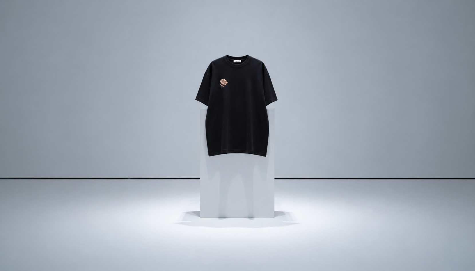 A black short-sleeve crewneck t-shirt with a small graphic on the left chest, displayed on a white pedestal in a minimalist gray studio setting.